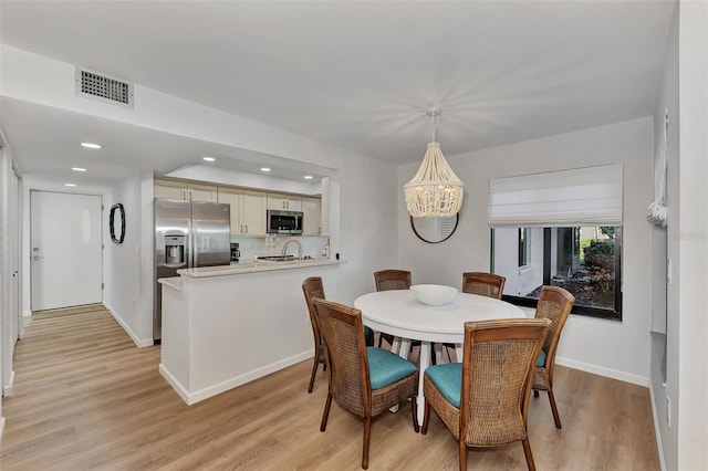 dining space with light hardwood / wood-style floors, an inviting chandelier, and sink