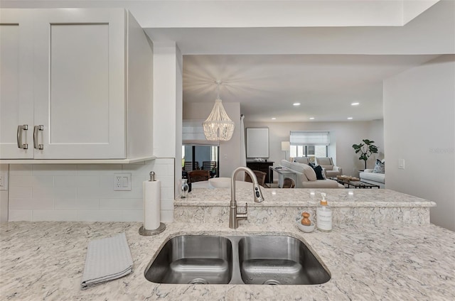 kitchen featuring backsplash, an inviting chandelier, white cabinets, sink, and light stone countertops