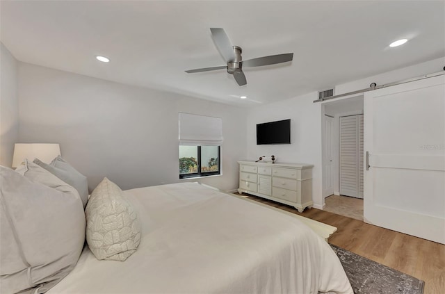 bedroom with light wood-type flooring, a barn door, a closet, and ceiling fan