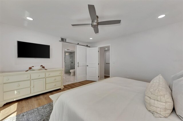 bedroom with a barn door, ceiling fan, light hardwood / wood-style flooring, and ensuite bath