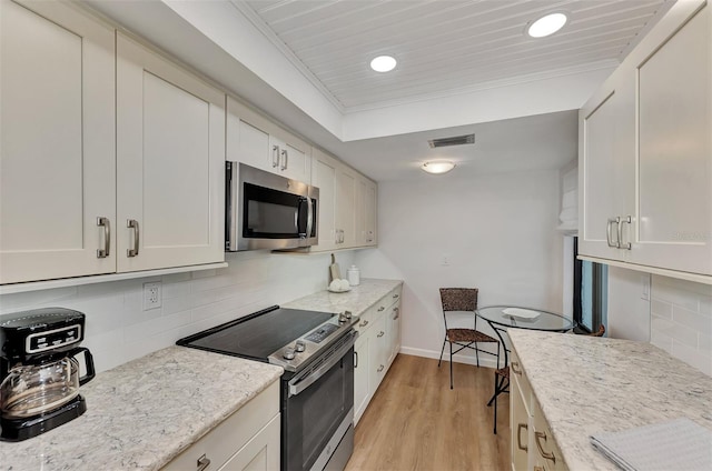 kitchen featuring light stone counters, light hardwood / wood-style flooring, backsplash, white cabinets, and appliances with stainless steel finishes