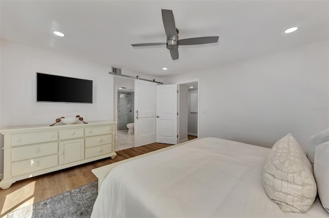 bedroom with hardwood / wood-style flooring, ensuite bathroom, ceiling fan, and a barn door