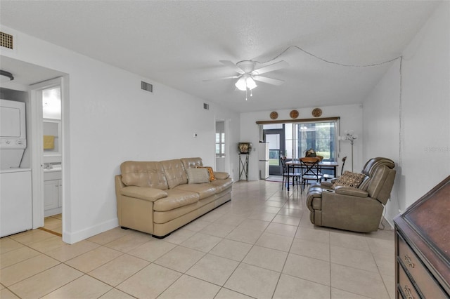 living room with a textured ceiling, ceiling fan, light tile patterned flooring, and stacked washer / drying machine