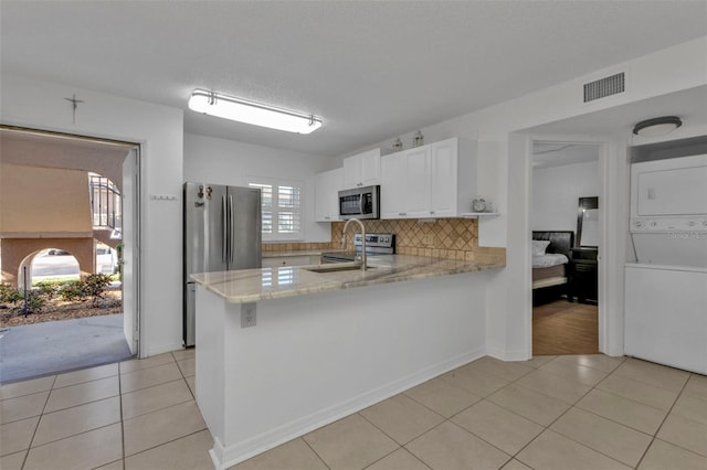 kitchen with kitchen peninsula, stainless steel appliances, light tile patterned floors, white cabinets, and stacked washer and dryer