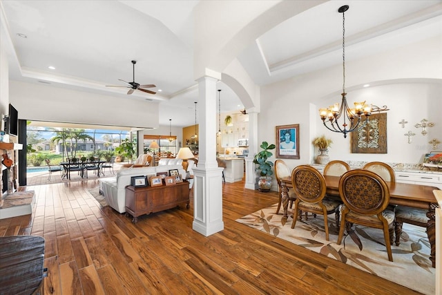 dining space with ceiling fan with notable chandelier, ornate columns, a towering ceiling, a tray ceiling, and wood-type flooring