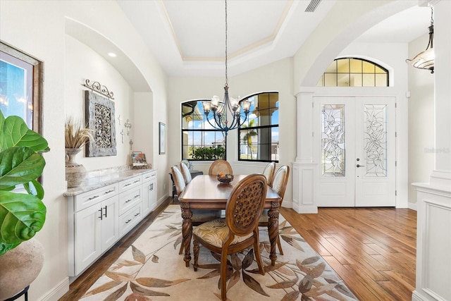 dining area with an inviting chandelier, a raised ceiling, wood-type flooring, and french doors