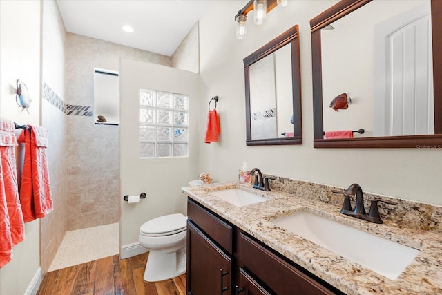 bathroom featuring hardwood / wood-style flooring, vanity, toilet, and tiled shower