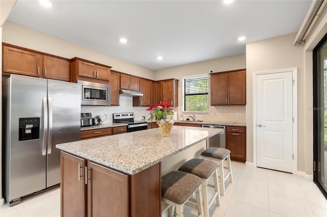 kitchen with light stone countertops, appliances with stainless steel finishes, sink, a kitchen island, and a breakfast bar area