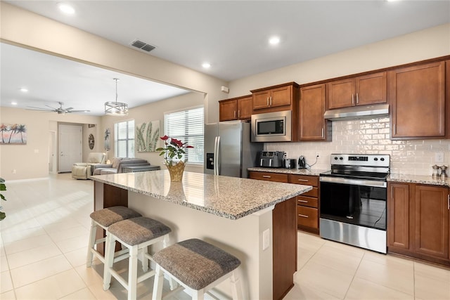 kitchen with a center island, hanging light fixtures, ceiling fan, appliances with stainless steel finishes, and a breakfast bar area