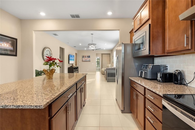 kitchen with light stone countertops, ceiling fan, stainless steel microwave, a kitchen island, and exhaust hood