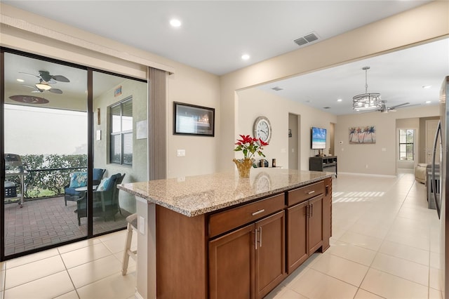 kitchen with light stone counters, ceiling fan, pendant lighting, a kitchen island, and light tile patterned flooring