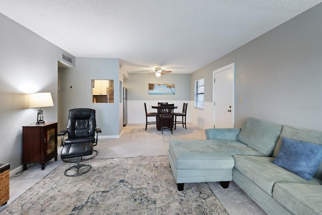 carpeted living room featuring ceiling fan and a textured ceiling