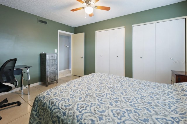 bedroom with ceiling fan, light tile patterned floors, a textured ceiling, and two closets