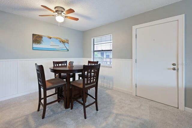 dining space with a textured ceiling, ceiling fan, and light colored carpet