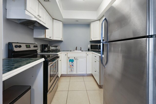 kitchen with light tile patterned floors, appliances with stainless steel finishes, tile counters, white cabinets, and sink