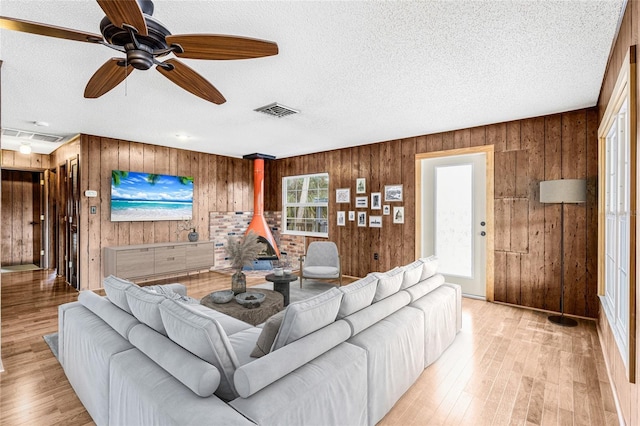 living room with a wood stove, a textured ceiling, light hardwood / wood-style flooring, and wood walls