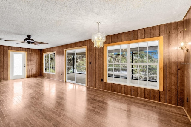 empty room featuring hardwood / wood-style floors, ceiling fan with notable chandelier, wood walls, and a textured ceiling