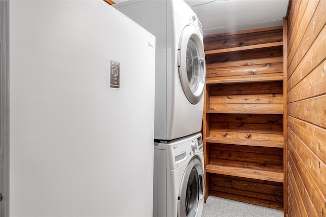 clothes washing area featuring stacked washer / dryer and wooden walls