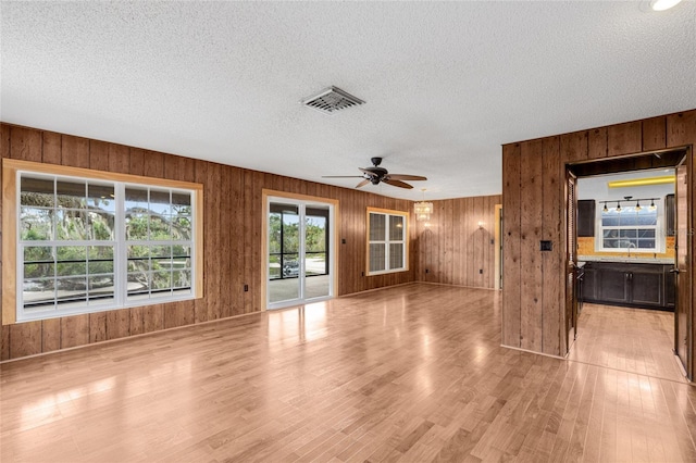 unfurnished living room featuring ceiling fan, sink, a textured ceiling, wooden walls, and light wood-type flooring