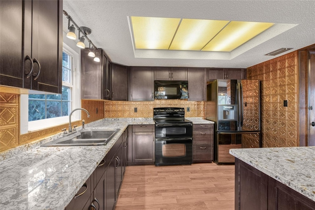 kitchen with sink, light hardwood / wood-style floors, a tray ceiling, dark brown cabinets, and black appliances