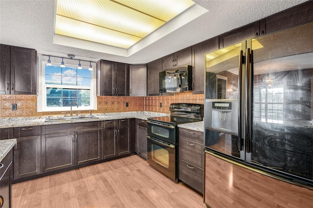 kitchen featuring light stone countertops, light wood-type flooring, dark brown cabinets, sink, and black appliances