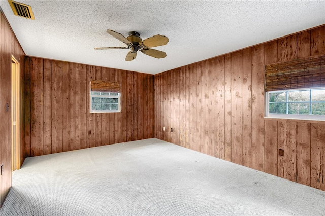 empty room with carpet flooring, a textured ceiling, ceiling fan, and wooden walls