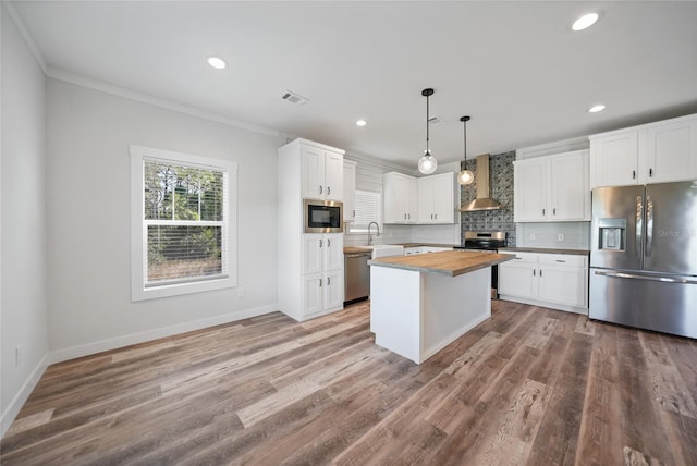 kitchen with white cabinets, wall chimney range hood, butcher block countertops, decorative light fixtures, and stainless steel appliances