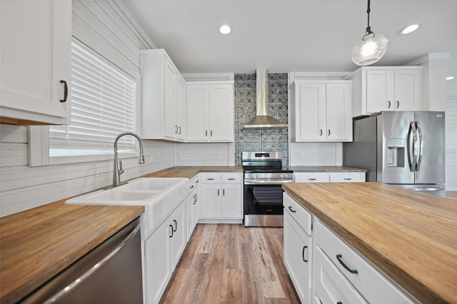 kitchen with wall chimney exhaust hood, wooden counters, decorative light fixtures, white cabinets, and appliances with stainless steel finishes