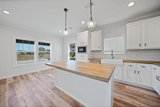 kitchen featuring built in microwave, sink, butcher block countertops, pendant lighting, and white cabinets