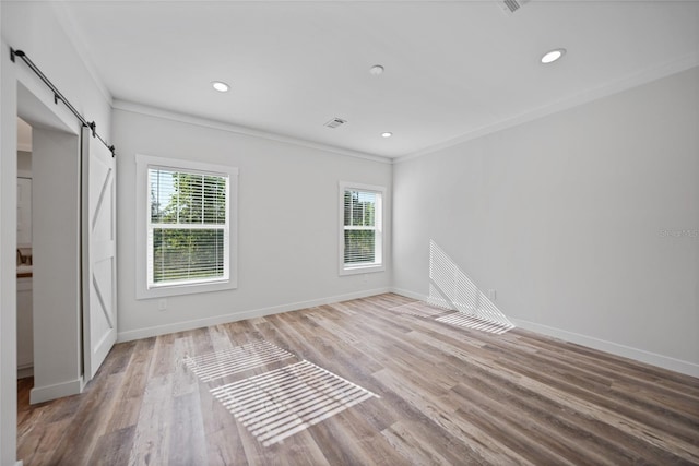 unfurnished room with wood-type flooring, a barn door, and crown molding