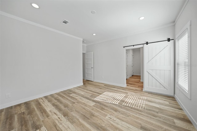 unfurnished bedroom with a barn door, light hardwood / wood-style floors, and crown molding