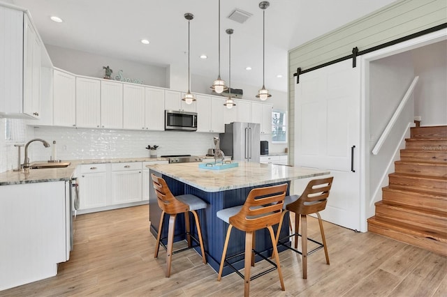 kitchen with sink, stainless steel appliances, a barn door, pendant lighting, and white cabinets