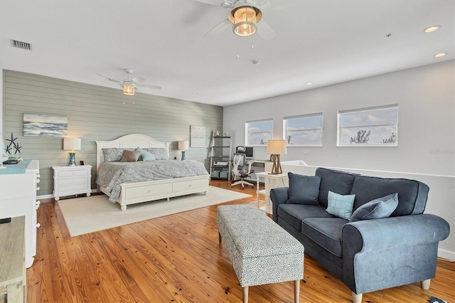 bedroom featuring light wood-type flooring, ceiling fan, and wood walls