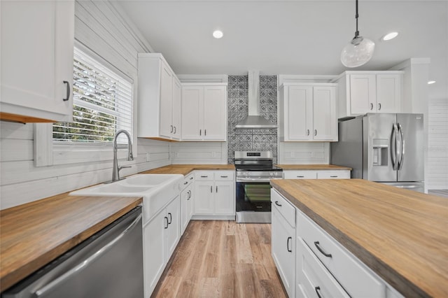 kitchen with wall chimney range hood, wooden counters, decorative light fixtures, white cabinets, and appliances with stainless steel finishes