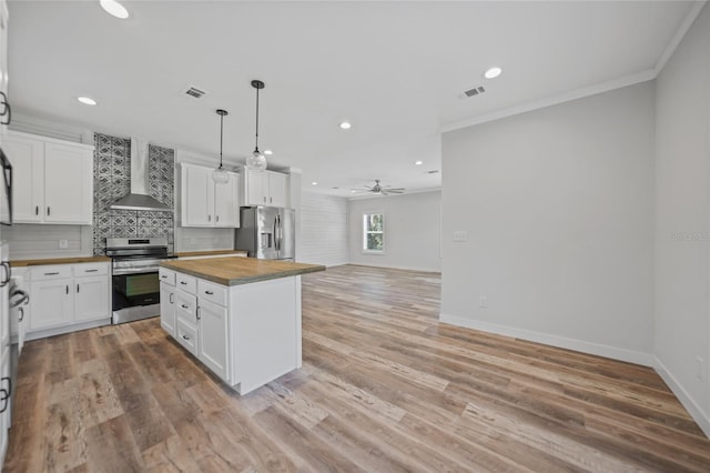 kitchen featuring butcher block counters, white cabinetry, wall chimney range hood, a kitchen island, and appliances with stainless steel finishes