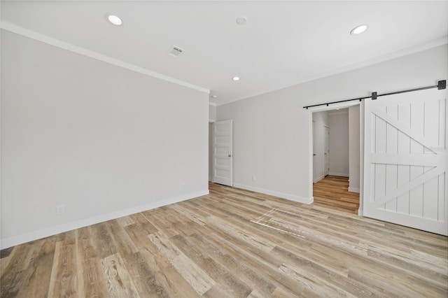 unfurnished bedroom with a barn door, light hardwood / wood-style floors, and ornamental molding