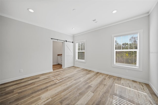 unfurnished bedroom featuring a barn door, light hardwood / wood-style floors, and crown molding