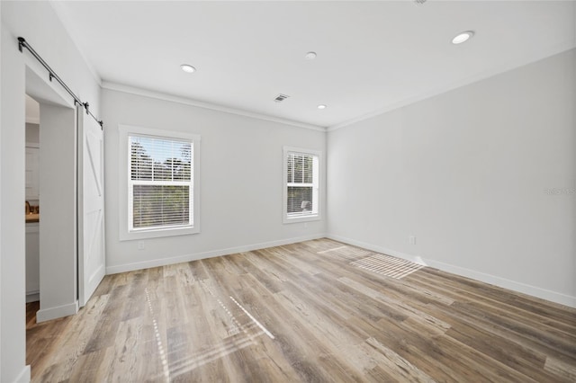 empty room featuring a barn door, light wood-type flooring, and ornamental molding