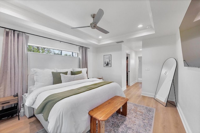 bedroom with light hardwood / wood-style floors, a raised ceiling, ceiling fan, and crown molding