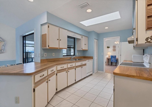 kitchen with white appliances, exhaust hood, sink, a skylight, and kitchen peninsula