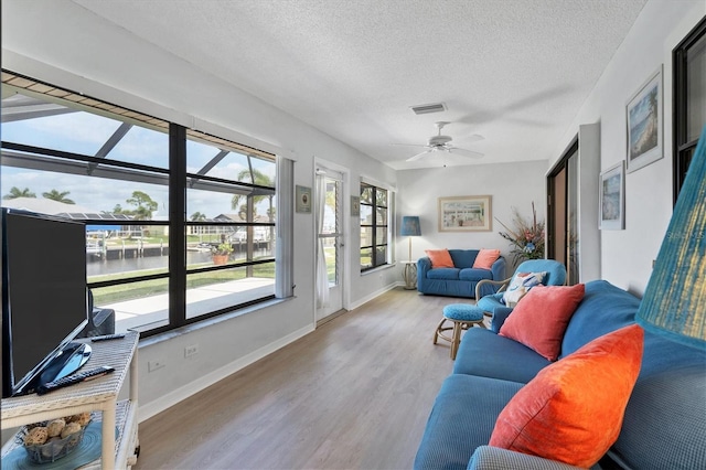 living area with visible vents, a ceiling fan, a textured ceiling, wood finished floors, and baseboards