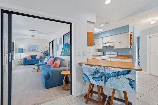 kitchen with white cabinetry, kitchen peninsula, white appliances, a breakfast bar, and light tile patterned flooring