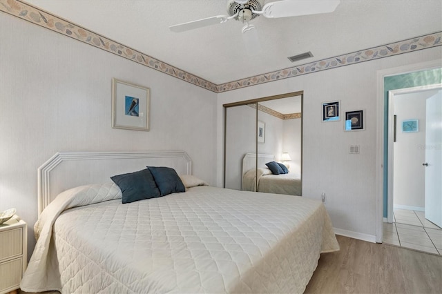 bedroom featuring a ceiling fan, wood finished floors, visible vents, baseboards, and a closet