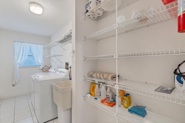 washroom featuring washing machine and clothes dryer, laundry area, a sink, a textured ceiling, and tile patterned floors