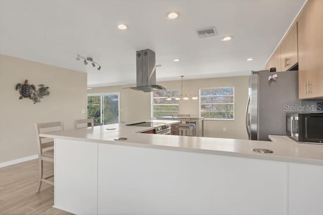 kitchen featuring island exhaust hood, pendant lighting, kitchen peninsula, and a breakfast bar area