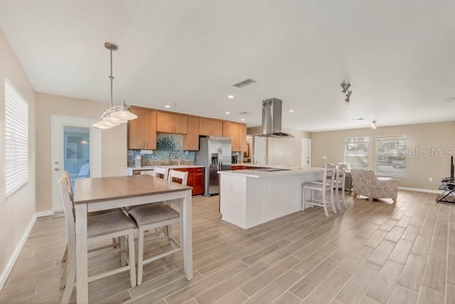 kitchen featuring stainless steel refrigerator with ice dispenser, backsplash, pendant lighting, plenty of natural light, and range hood