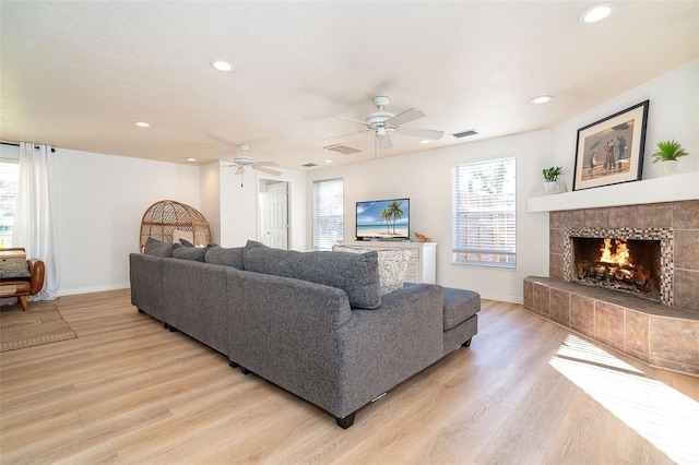 living room with light wood-type flooring, ceiling fan, and a tiled fireplace