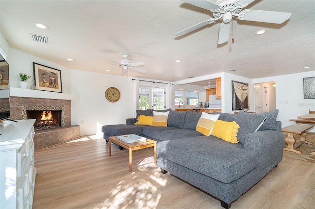 living room with ceiling fan, a fireplace, and light hardwood / wood-style flooring