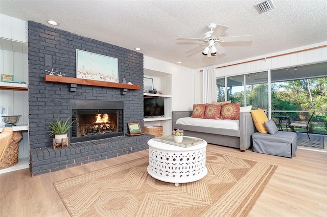 living room with ceiling fan, light hardwood / wood-style flooring, a textured ceiling, and a brick fireplace