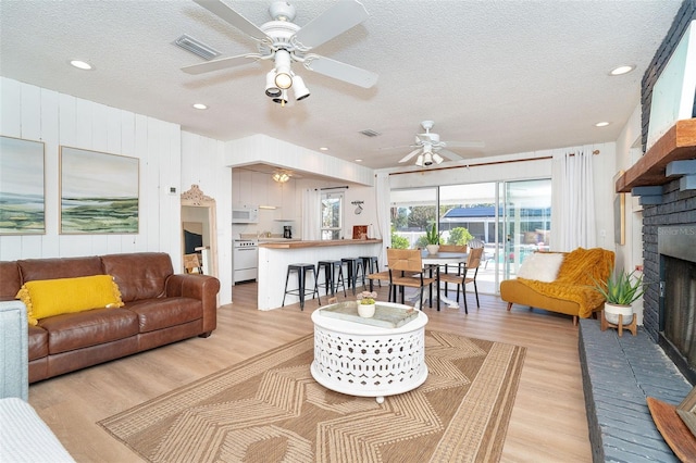 living room with a textured ceiling, ceiling fan, light hardwood / wood-style floors, and a fireplace